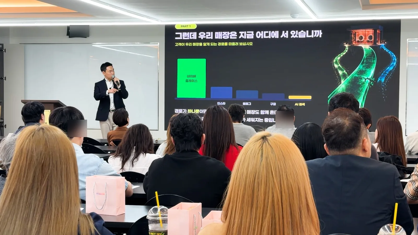 고객이 매장을 알게 되는 경로를 막대그래프로 보여 주는 슬라이드 앞에서 마이크를 들고 설명하는 유준식