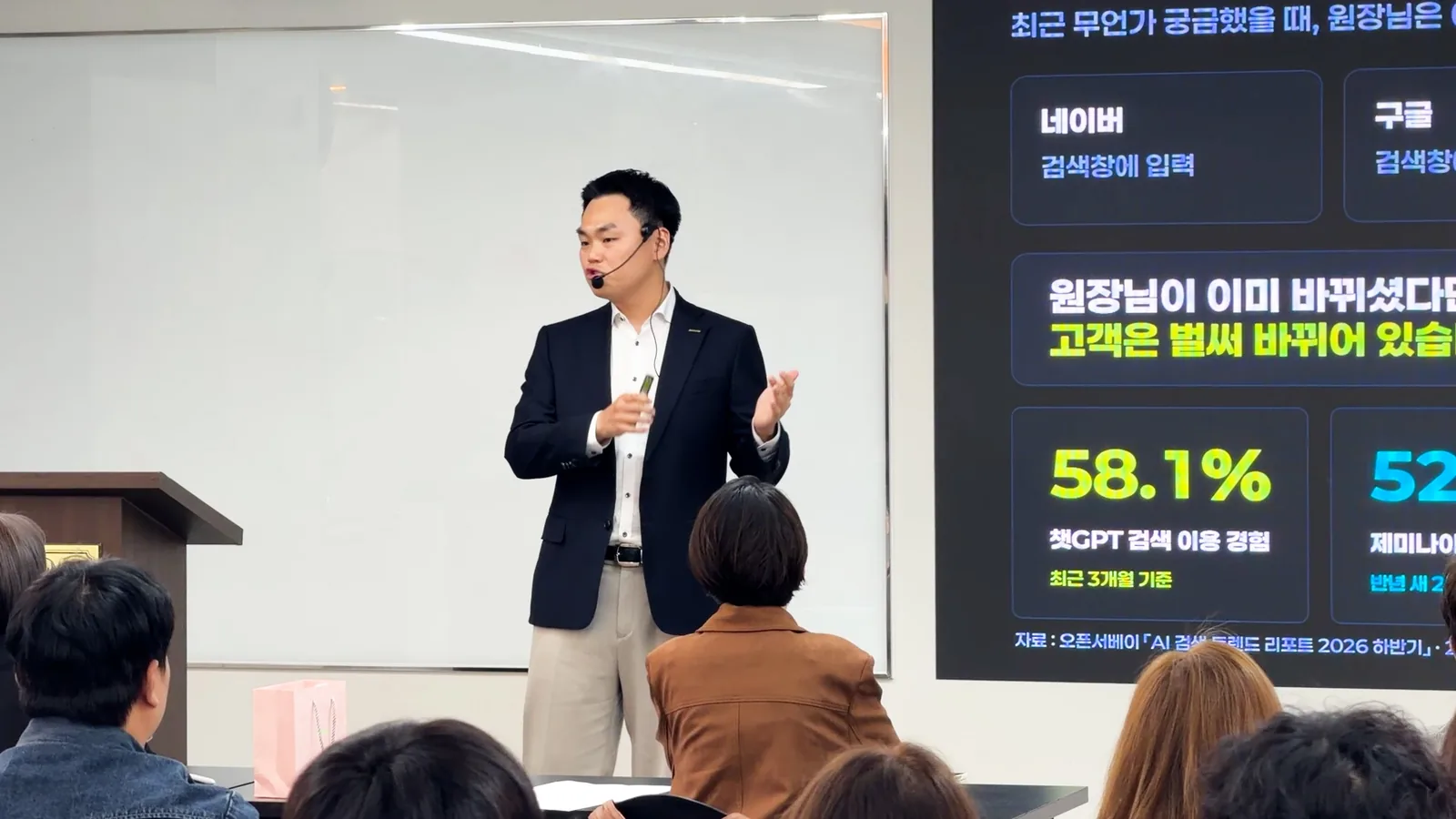 AI 검색 이용 통계 슬라이드를 배경으로 두 손을 들어 설명하는 유준식